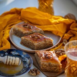Close-up of baklava pieces with honey and walnuts, surrounded by orange textiles.