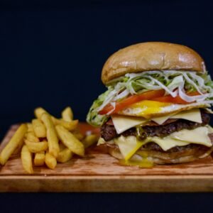 Tasty double cheeseburger with fries on a wooden board against a black background.