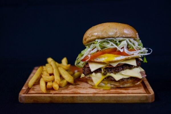 Tasty double cheeseburger with fries on a wooden board against a black background.