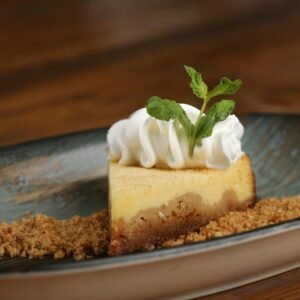 A mouthwatering slice of cheesecake with whipped cream and mint garnish is beautifully plated.