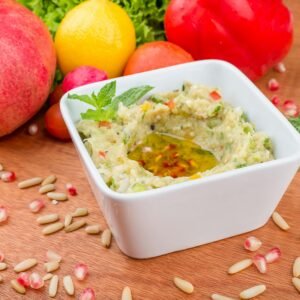 Close-up of baba ghanoush served with mint, olive oil, and fresh veggies.